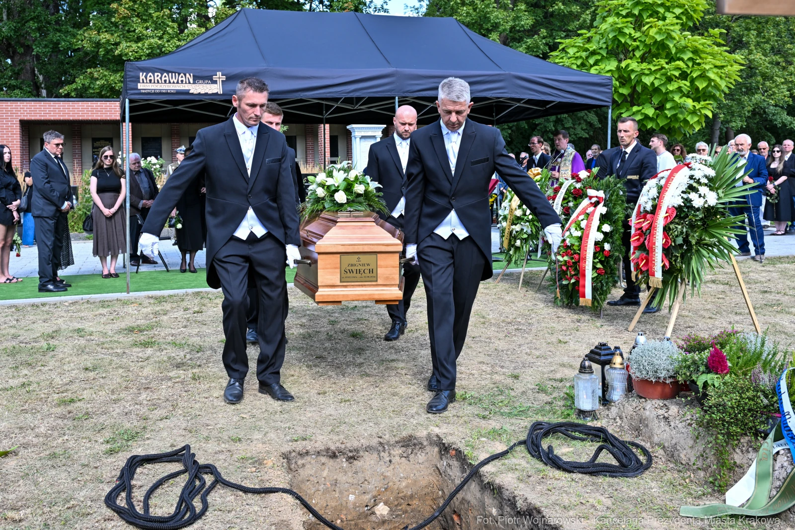Pogrzeb z trumną niesioną przez mężczyzn w garniturach, otoczoną kwiatami i żałobnikami.  Autor: Piotr Wojnarowski