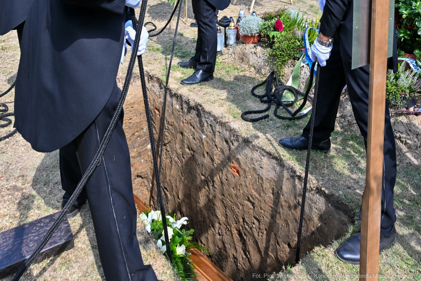 Pogrzeb, mężczyźni w garniturach trzymający liny nad grobem.  Autor: Piotr Wojnarowski