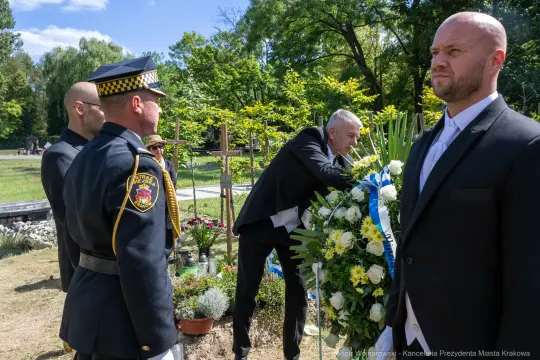 Ceremonia składania wieńca na grobie, obecność policji i osób w żałobie.