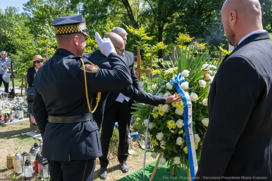 Ceremonia pogrzebowa z obecnością strażnika i kwiatów na grobie.