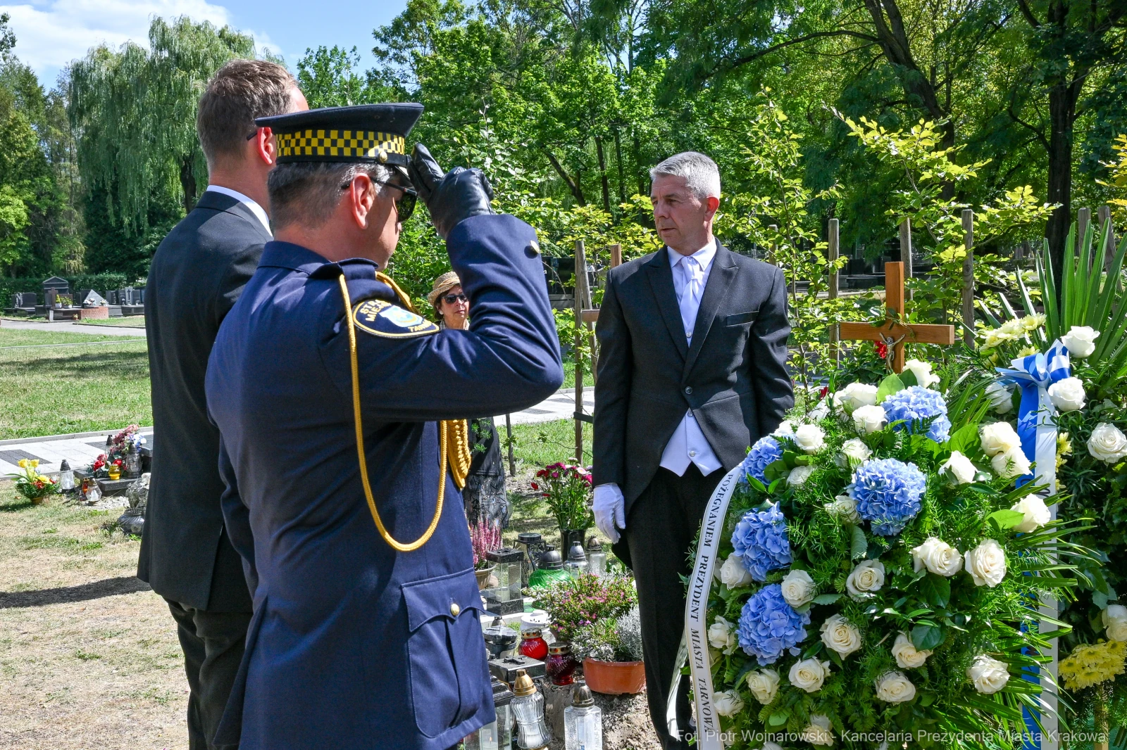 Ceremonia pogrzebowa z obecnością policjanta i mężczyzny w garniturze, kwiaty na grobie.  Autor: Piotr Wojnarowski