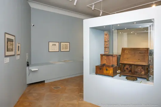 Wnętrze muzeum z wystawą rysunków i drewnianych skrzyń.