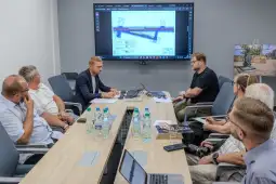 Spotkanie zespołu przy stole konferencyjnym z prezentacją projektu na ekranie.