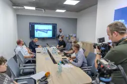 Konferencja prasowa z prezentacją projektu na ekranie oraz dziennikarzami z kamerami.