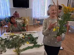 Kobiety zbierają i układają kwiaty oraz zioła w sali.