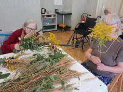 Dwie osoby tworzą bukiety z suszonych kwiatów w świetlicy.