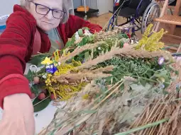 Kobieta w okularach tworzy bukiet z suszonych kwiatów i ziół.