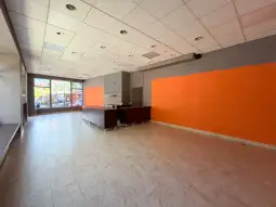 Pusty lokal z pomarańczową ścianą i jasnymi kafelkami na podłodze.