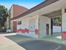 Budynek z muralem w czerwonym kolorze, w tle widoczny parking i inne budynki.