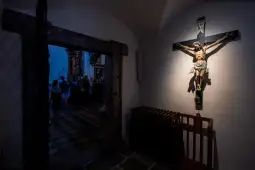 Krucyfiks na ścianie w kościele, w tle widoczni ludzie.