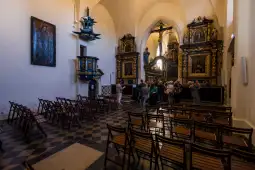 Wnętrze kościoła z drewnianymi ławkami i bogato zdobionymi ołtarzami. Grupa ludzi zwiedza.