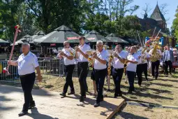 Orkiestra dęta w trakcie parady, grająca na festynie w słoneczny dzień.