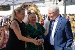 Uścisk dłoni między dwiema kobietami a mężczyzną, w tle tłum i dekoracje festiwalowe.