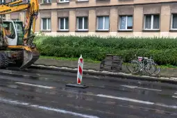 Maszyna budowlana obok rowerów i znaku drogowym na mokrej nawierzchni.