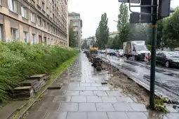 Remont chodnika przy ruchliwej ulicy, widoczne prace budowlane i pojazdy.