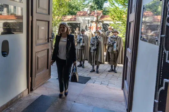 Kobieta wchodzi do budynku, w tle strażnicy w mundurach.