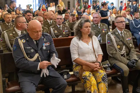 Uczestnicy ceremonii siedzący w kościele, w mundurach wojskowych i cywilnych.