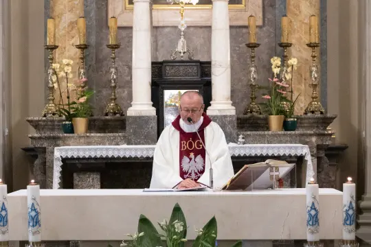 Ksiądz odprawiający mszę w kościele, z ołtarzem w tle.