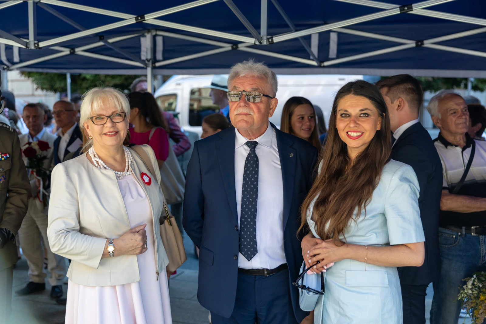Trzy osoby w eleganckich strojach, uśmiechające się pod namiotem.  Autor: Bogusław Świerzowski