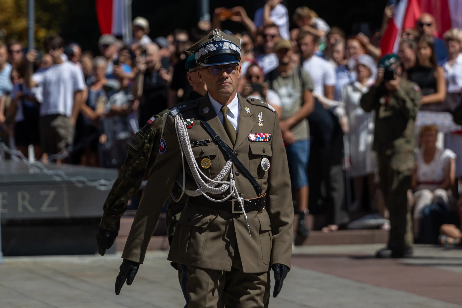 Mężczyzna w mundurze wojskowym podczas ceremonii, w tle tłum z flagami.  Autor: Bogusław Świerzowski