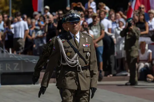 Mężczyzna w mundurze wojskowym podczas ceremonii, w tle tłum z flagami.