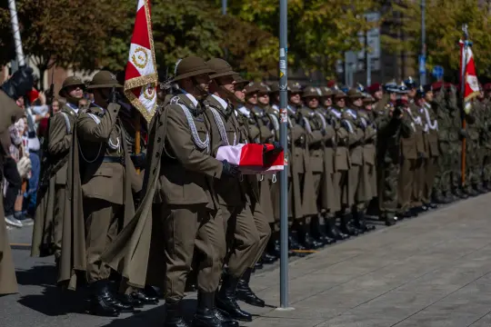 Żołnierze w mundurach podczas ceremonii, trzymający flagę i sztandary.