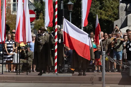 Uroczystość z flagami Polski, uczestnicy w strojach historycznych.