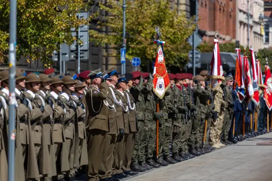 Uroczysta parada wojskowa z żołnierzami w mundurach i sztandarami.