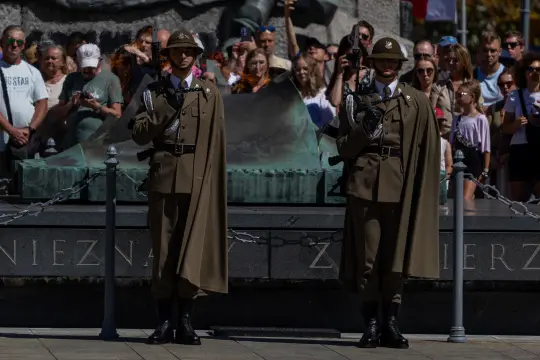 Dwaj żołnierze w mundurach ceremonialnych podczas uroczystości, tłum ludzi w tle.