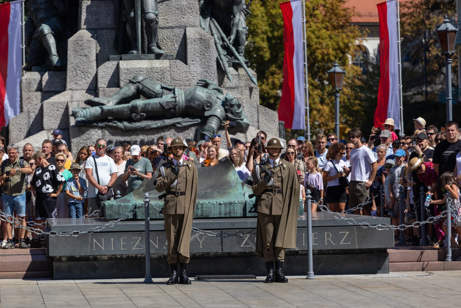 Dwaj żołnierze w mundurach stoją na straży przy pomniku Nieznanego Żołnierza, otoczeni przez tłum ludzi.  Autor: Bogusław Świerzowski