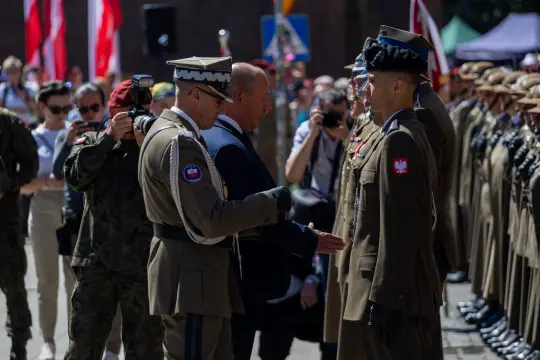 Ceremonia wojskowa z udziałem żołnierzy i oficjeli, w tle tłum ludzi.