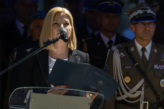 Kobieta przemawia do mikrofonu, w tle żołnierze w mundurach.