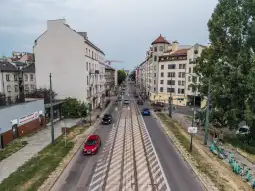 Ulica z samochodami i budynkami mieszkalnymi po obu stronach.