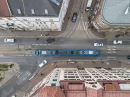Widok na ulicę z tramwajem, samochodami i budynkami w otoczeniu.
