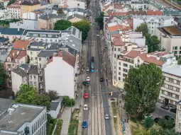 Widok na ulicę z tramwajami i samochodami, otoczoną budynkami mieszkalnymi.