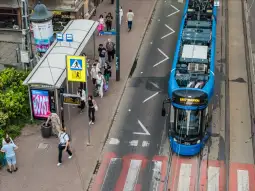 Tramwaj na przystanku, obok przejście dla pieszych i przechodnie.