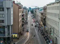 Ulica z samochodami, budynkami i pieszymi, w tle widoczny krajobraz miejski.