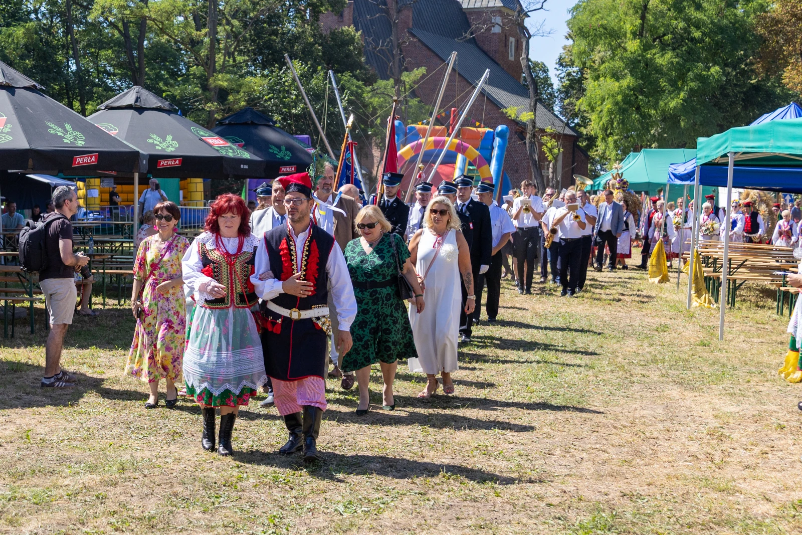 Grupa ludzi w tradycyjnych strojach ludowych idzie w kierunku festiwalu.  Autor: Bogusław Świerzowski