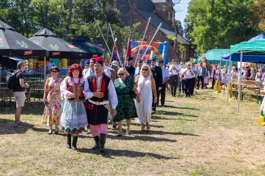 Grupa ludzi w tradycyjnych strojach ludowych idzie w kierunku festiwalu.