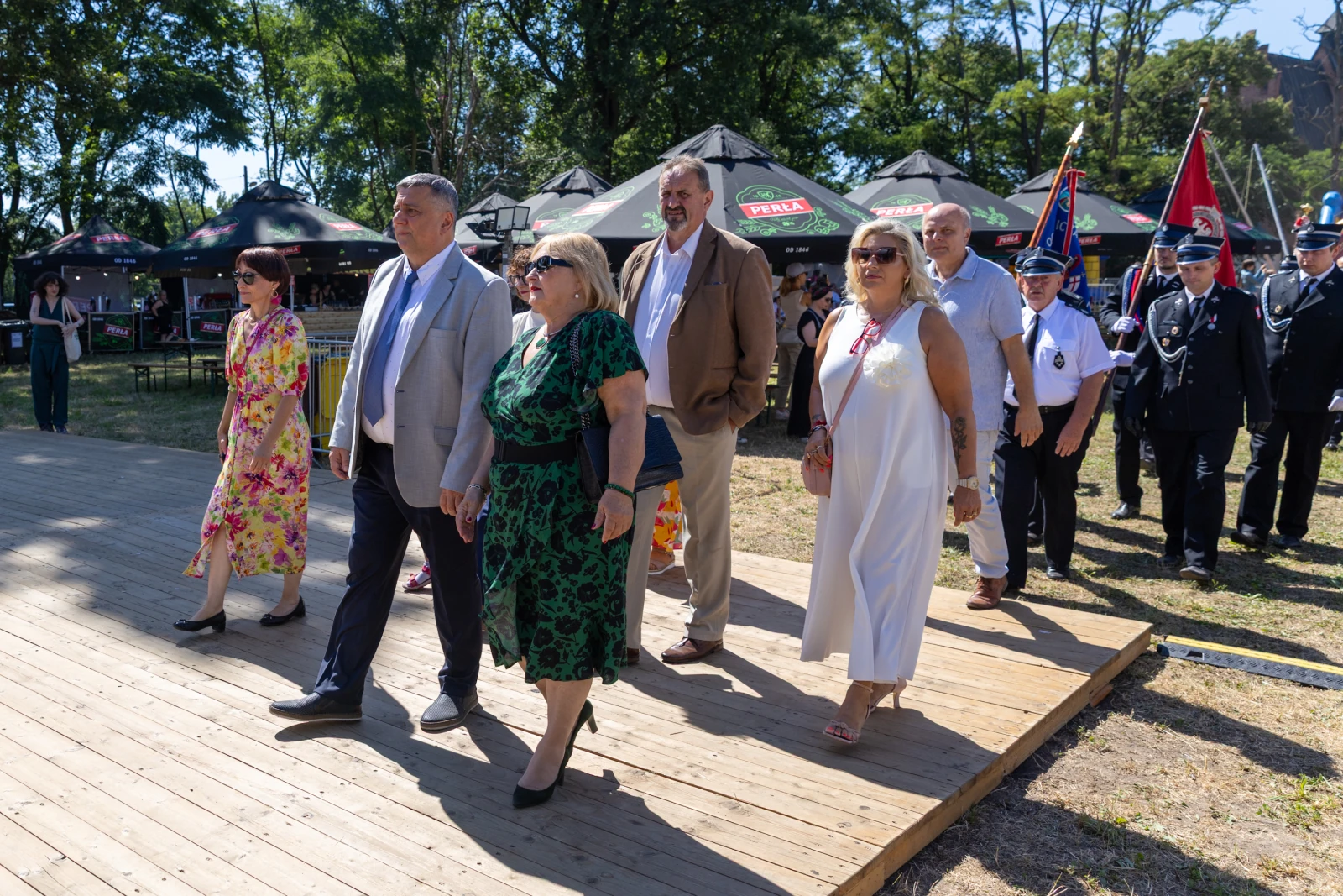 Grupa osób w eleganckich strojach idzie po drewnianym podłożu podczas wydarzenia plenerowego.  Autor: Bogusław Świerzowski