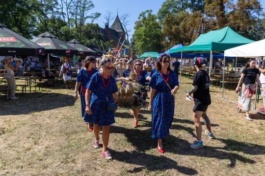 Grupa kobiet w kolorowych sukienkach niesie tradycyjną dekorację podczas festiwalu.