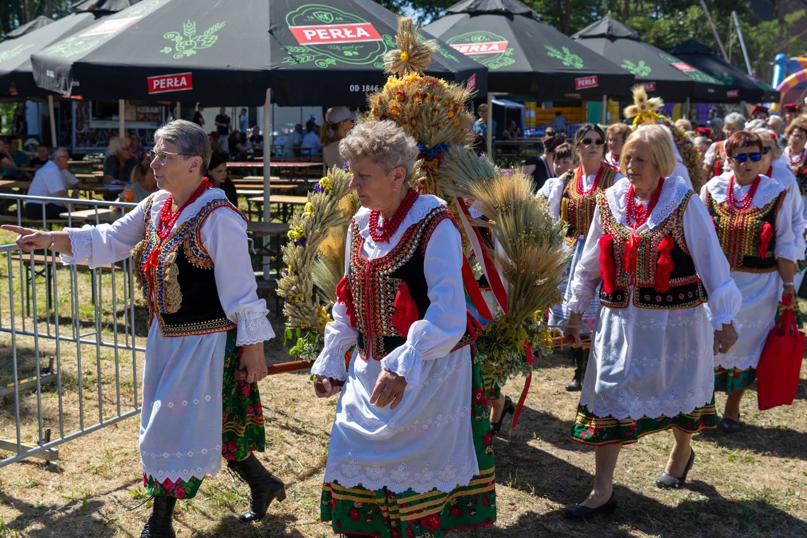 Grupa kobiet w tradycyjnych strojach ludowych, niosących ozdobę z zboża.  Autor: Bogusław Świerzowski