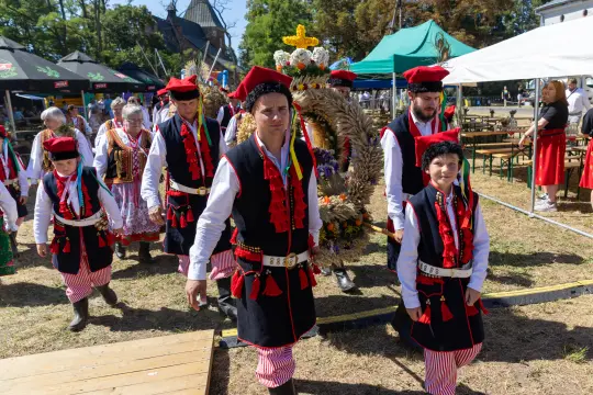 Grupa ludzi w tradycyjnych strojach ludowych niesie wieniec podczas festiwalu.