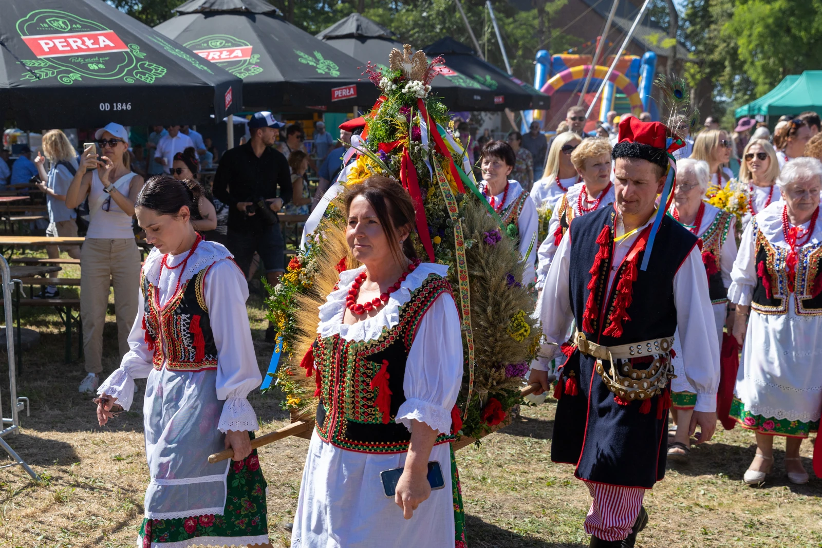 Grupa osób w tradycyjnych strojach ludowych niesie ozdobny wieniec podczas festynu.  Autor: Bogusław Świerzowski