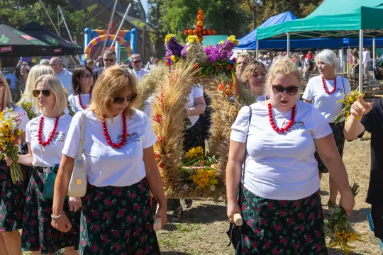 Grupa kobiet w tradycyjnych strojach niesie ozdobny wieniec podczas festiwalu.