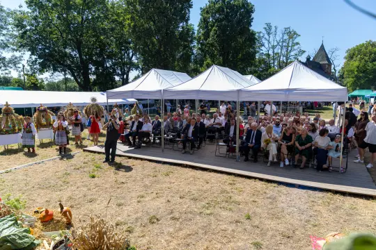 Impreza plenerowa z uczestnikami w strojach ludowych, namiotami i dekoracjami.