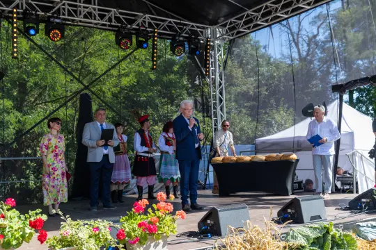 Uczestnicy wydarzenia na scenie, w tradycyjnych strojach, z chlebem na stole.