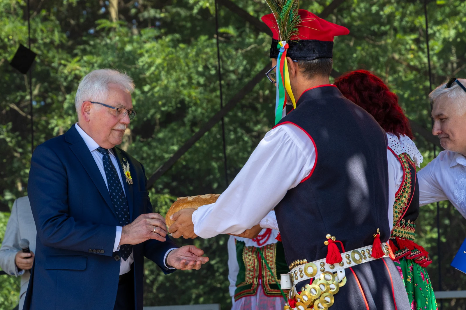 Mężczyzna w garniturze odbiera chleb od osoby w tradycyjnym stroju ludowym.  Autor: Bogusław Świerzowski
