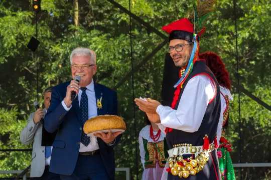 Mężczyźni w tradycyjnych strojach ludowych podczas uroczystości z chlebem.