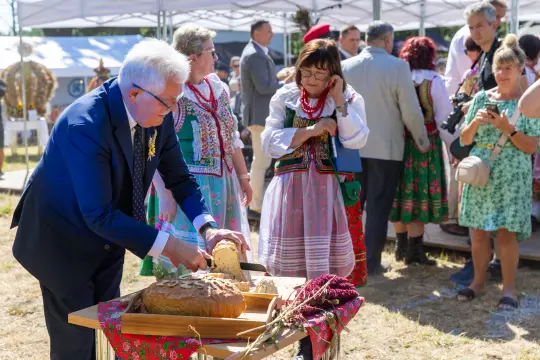 Mężczyzna kroi chleb, wokół niego ludzie w tradycyjnych strojach ludowych.